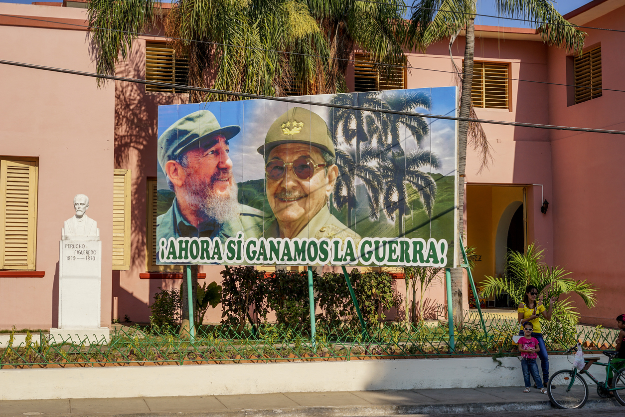 Santiago de Cuba, Cuba - January 12, 2016: Typical scene of one of streets in the center of Santiago de cuba - Big poster of Raul and Fidel Castro. people walking around. Santiago is the 2nd largest city in Cuba /Photo: iStock