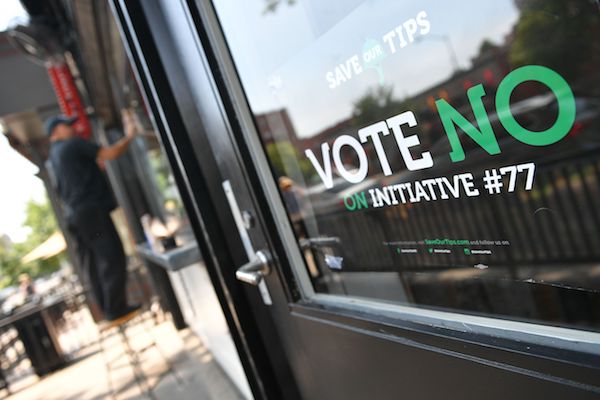 A man stands near a "vote no on Initiative #77" sign on June 18, 2018 in Washington, DC. - Washington, DC's upcoming primary election includes a ballot measure called Initiative 77, a policy to gradually raise the minimum wage that tipped workers receive. (MANDEL NGAN/AFP/Getty Images)