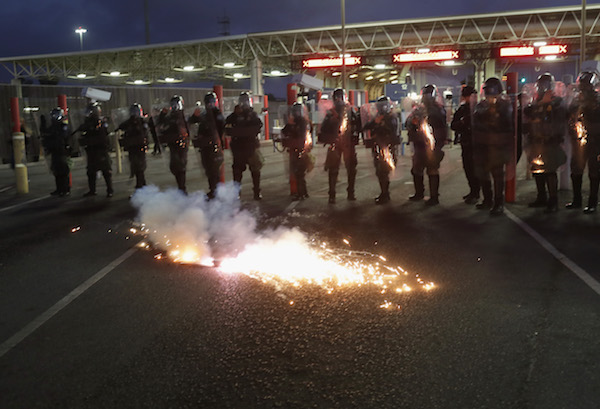 An artificial tear gas canister ignites as U.S. Customs and Border Protection (CBP) officers block the Otay Mesa port of entry from Mexico into the United States early on December 1, 2018 as seen from Tijuana, Mexico. CPB officers staged the crowd control training exercise, using riot gear and fake tear gas, in advance of a potential attempt by members of the migrant caravan to rush the border crossing. (Photo by John Moore/Getty Images)
