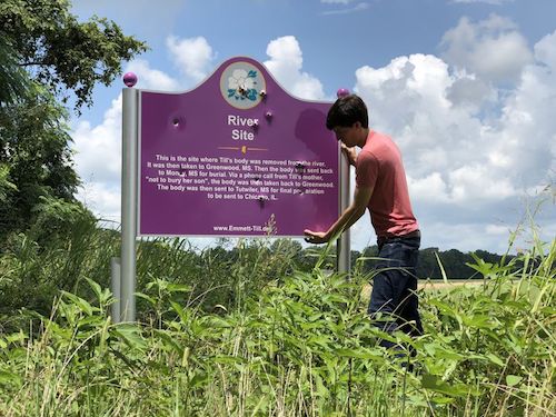Patrick Weems, executive director of the Emmett Till Memorial Commission of Tallahatchie County, stands July 20, 2019, with the vandalized sign marking the location where Emmett Till’s body was removed from the Tallatachie River near Glendora, Mississippi, in 1955. A 2018 photo has surfaced showing University of Mississippi students holding rearms and posing next to the sign damaged by bullet holes. (Courtesy of Emmett Till Interpretive Center)