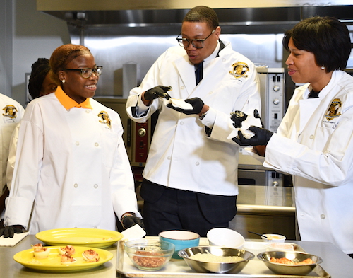 DCPS Chancellor Lewis Ferebee (center) and D.C. Mayor Muriel Bowser (right) sample some treats, courtesy of Ballou Senior High School students in the Southeast-based school's culinary arts academy. (Anthony Tilghman/The Washington Informer)