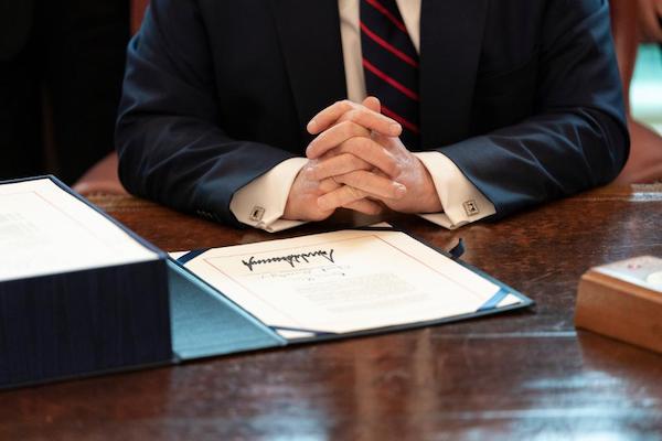 President Trump signs the coronavirus stimulus relief package in the Oval Office at the White House on March 27. (Courtesy of the White House)