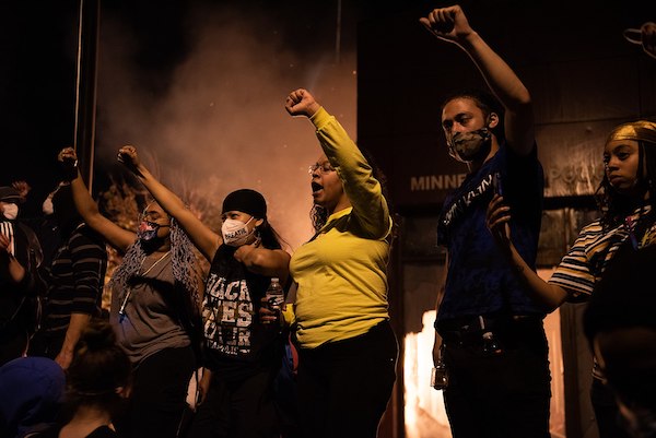 Demonstrators protesting the police-related death of George Floyd stand with fists raised outside the burning Minneapolis 3rd Police Precinct on May 28. (Courtesy of Wikimedia Commons)