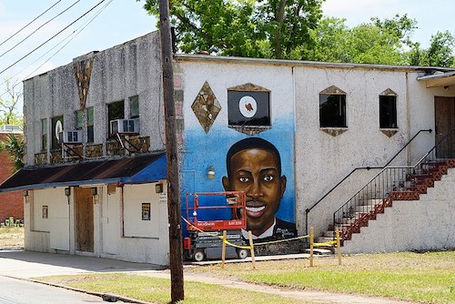 A mural of Ahmaud Arbery at 1621 Albany Street, Brunswick, Georgia. Arbery was shot to death in February 2020. This building is scheduled to house the Brunswick African American Cultural Center. The mural was painted by Marvin Meeks in May 2020. (Courtesy of Wikimedia Commons)