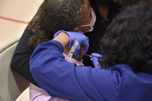 Gianna Piazza, 7, snuggles beside her mother as she receives a coronavirus vaccine in her right arm at a clinic inside Judge Sylvania Woods Elementary School in Glenarden, Maryland, on Nov. 8. (Robert R. Roberts/The Washington Informer)