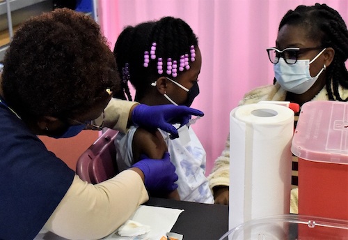 Anna Otto-Quarshie, 8, receives a coronavirus vaccine as her mother, Faith Quarshie, holds her hand at the Sports and Learning Complex in Landover, Maryland, on Nov. 13. (Robert R. Roberts/The Washington Informer)