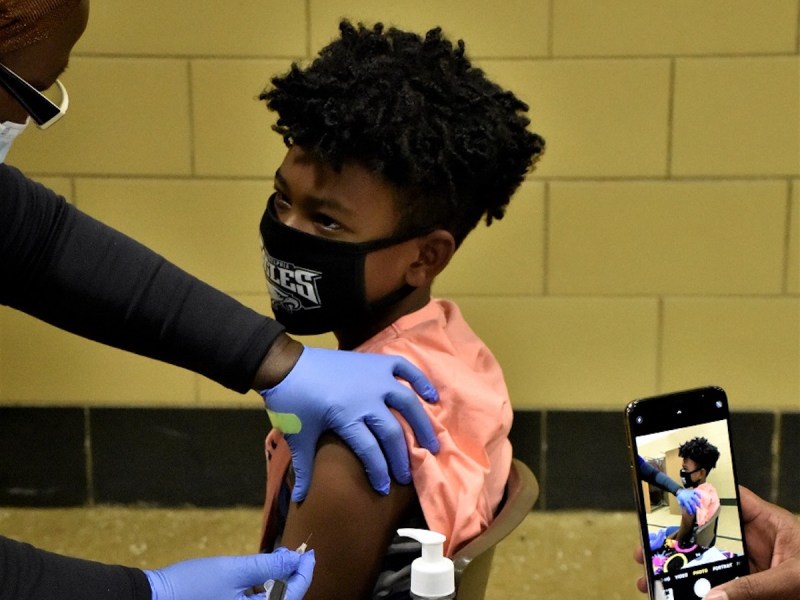 **FILE** Dyson S. Barnes, 9, receives a coronavirus vaccination at a clinic inside Capitol Heights Elementary School in Capitol Heights, Maryland, on Nov. 17 as his mother, Shannon Duckett-Barnes, captures the moment on her cellphone. (Robert R. Roberts/The Washington Informer)