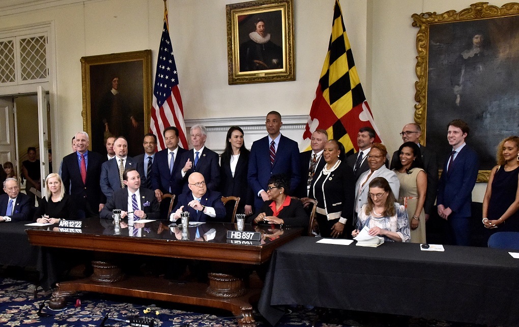 Maryland Gov. Larry Hogan (bottom row, 4th from left) sits between Senate President Bill Ferguson (left) and House Speaker Adrienne Jones after signing legislation for Maryland Stadium Authority to issue bonds for economic development project in Prince George’s County, while Authority and Prince George’s officials stand behind them to pose for a picture during a bill-signing ceremony at the State House in Annapolis on April 12. (Robert R. Roberts/The Washington Informer)