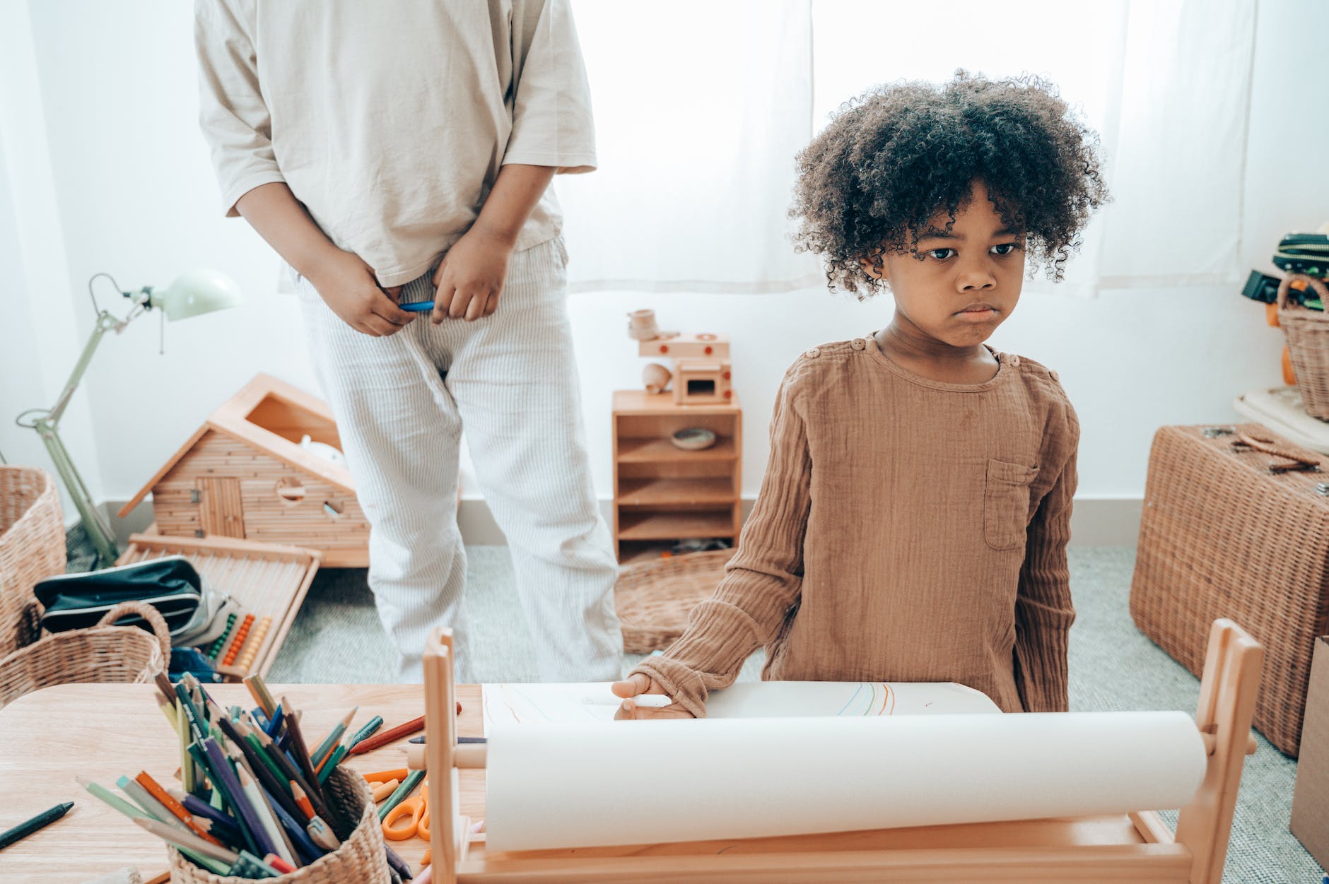 sad african american kid with paper sheet near crop sibling