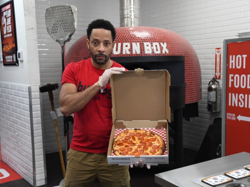 Burn Box owner Ryan Whitfield holds a pepperoni pizza, fresh out of the brick oven. (Anthony Tilghman/The Washington Informer)