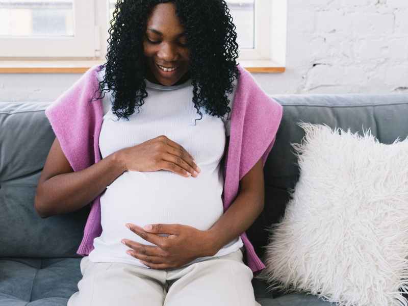 happy pregnant black woman sitting on couch