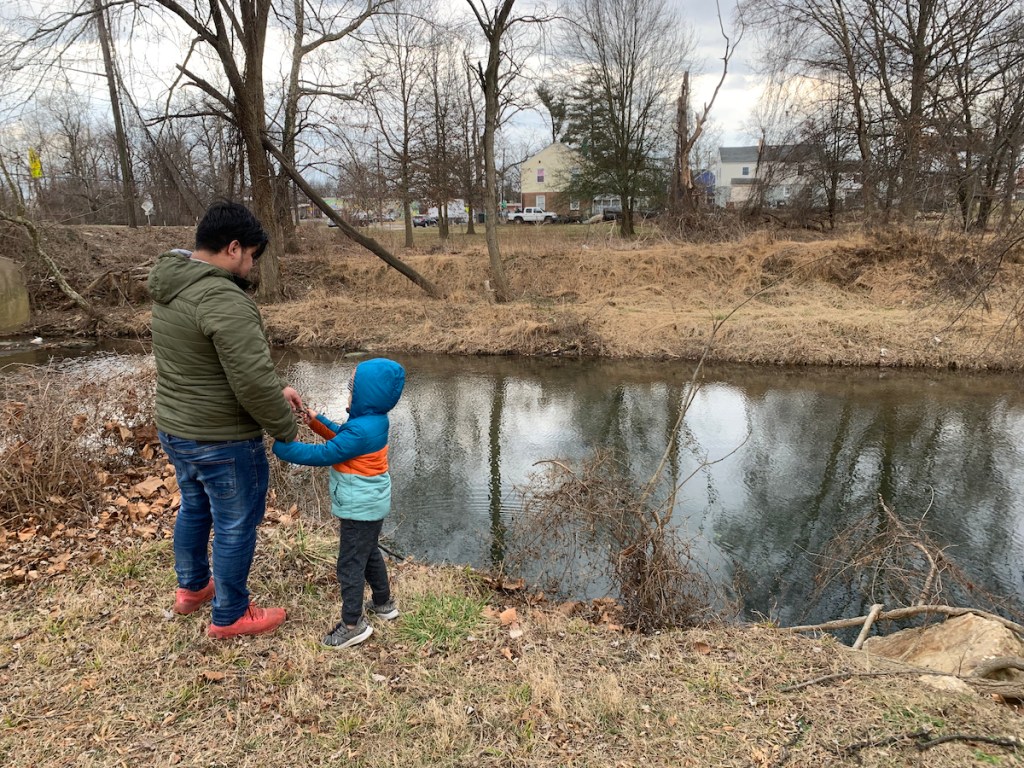 An adult and child throw sticks into Sligo Creek while waiting for the bus.