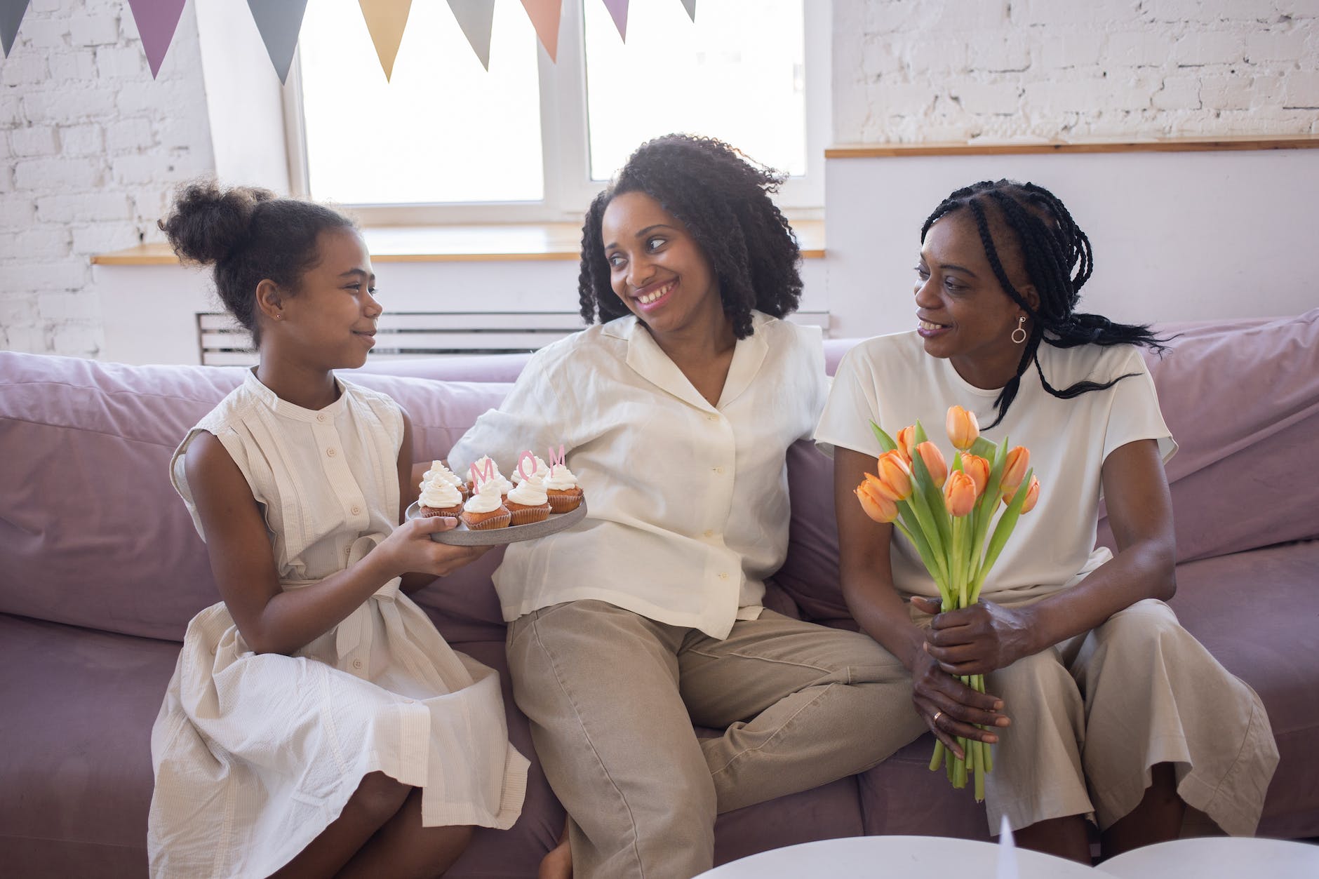a child holding a plate of cupcakes sitting next to two women
