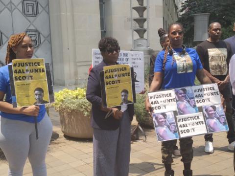 TaiJoh'e Scott, Marion Gray-Hopkins and Alanta Scott stand in front of the U.S. Department of Justice to demand U.S. Marshals Service's body-camera footage from the police-involved shooting of Alaunte Scott. (Sam P.K. Collins/The Washington Informer)