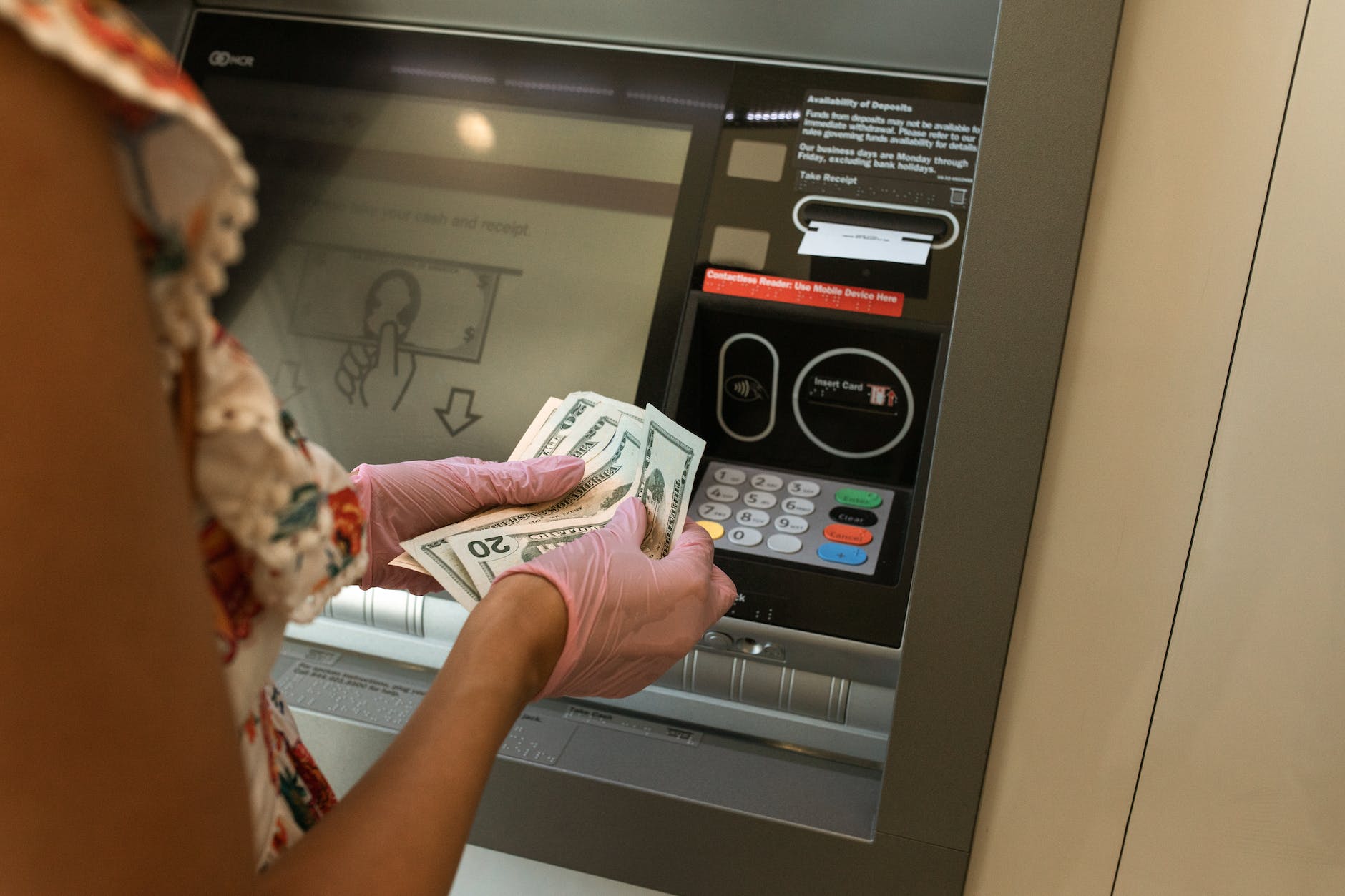 person counting money in front of atm
