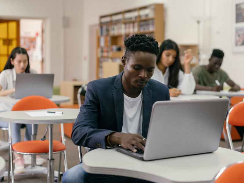 a man wearing a blue suit jacket sitting at a desk using a silver laptop