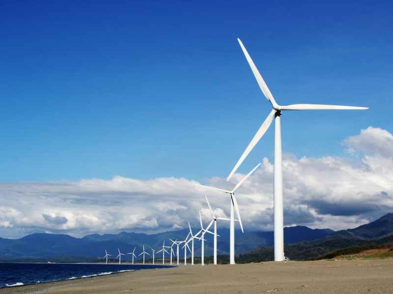 white wind turbines on gray sand near body of water