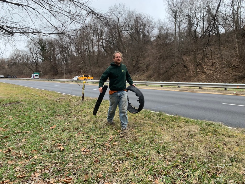 Nathan Harrington of Ward 8 Woods carries a broken tire visible from the road to his truck. (Kayla Benjamin/The Washington Informer)