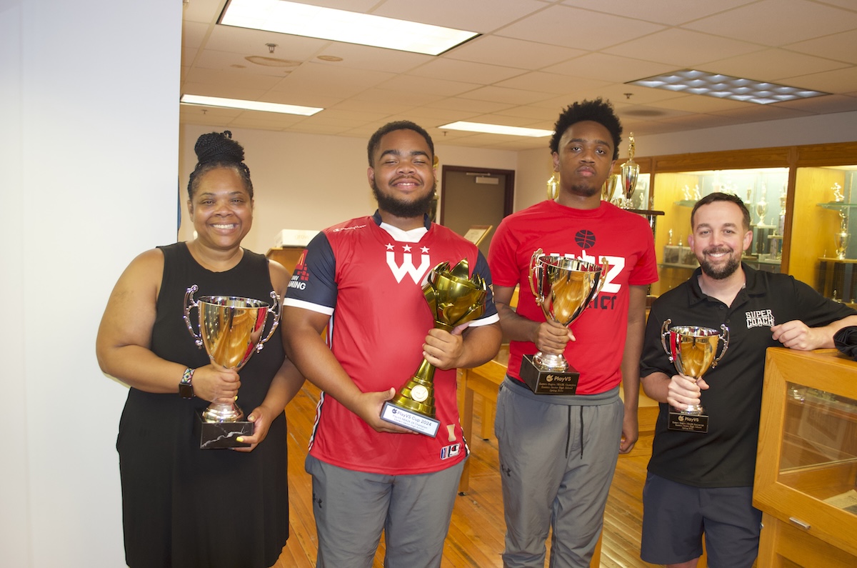 From left: Sherry Williams, Tyler Frost, Taylor Frost and coach Lee James pose with championship trophies in Eastern High's trophy room. (Demarco Rush/The Washington Informer)